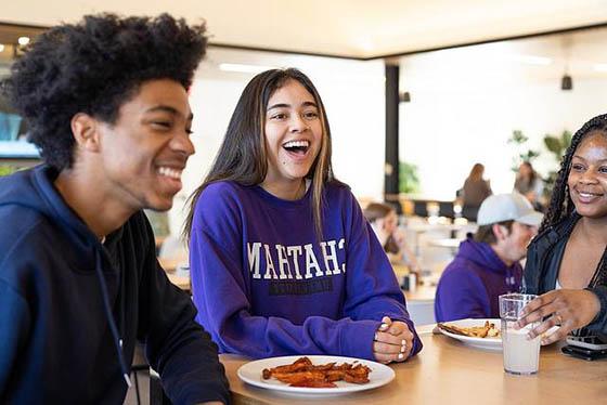 A group of three students smile and laugh at a dining hall table