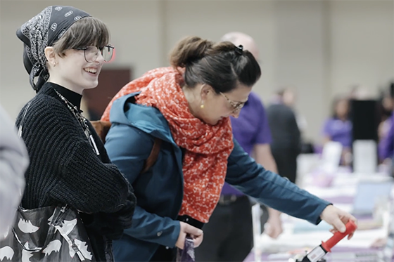 A student smiles at an unseen volunteer, who is seated behind an information table