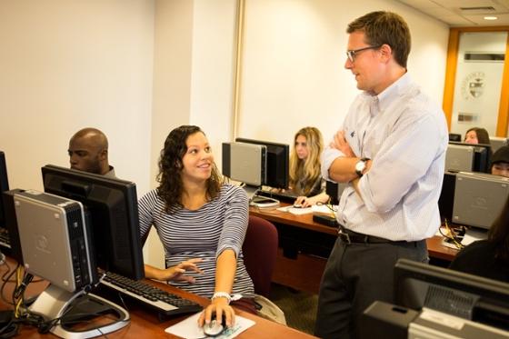 Photo of Chatham University students in a computer lab, with a male faculty member speaking with a female student